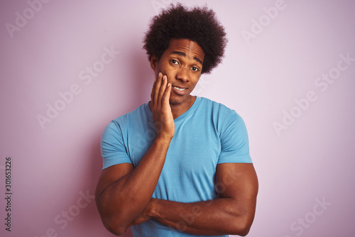 African american man with afro hair wearing blue t-shirt standing over isolated pink background thinking looking tired and bored with depression problems with crossed arms.