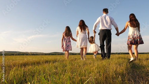 mother, father and little daughter with sisters walking in field in the sun. Happy young family. Children, dad and mom play in meadow in the sunshine. concept of happy family.