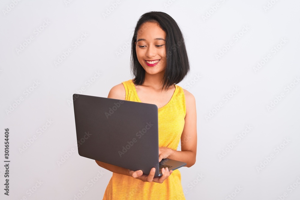 Naklejka premium Young beautiful chinese woman using laptop standing over isolated white background with a happy face standing and smiling with a confident smile showing teeth
