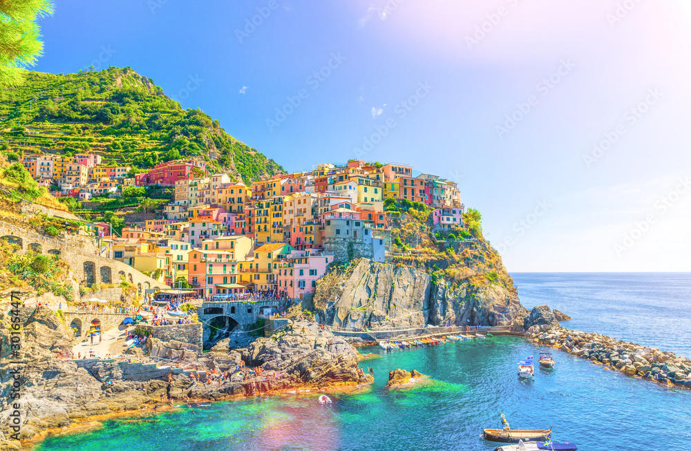 Manarola traditional typical Italian village in National park Cinque Terre, colorful multicolored buildings houses on rock cliff, fishing boats on water, blue sky background, La Spezia, Liguria, Italy
