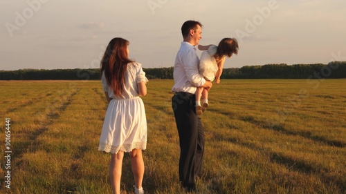 Happy dad carries a little daughter in his arms and plays with his mother on the field. Parents play with the child for a walk. Family life concept. Teamwork. Concept of a happy childhood.