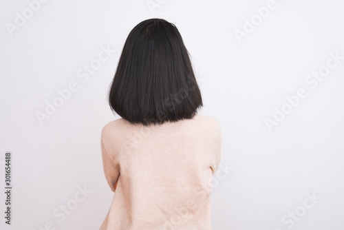 Young chinese woman wearing turtleneck sweater standing over isolated white background standing backwards looking away with crossed arms