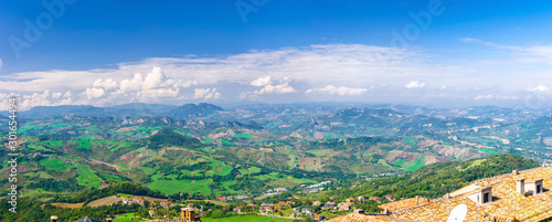 Aerial top panoramic view of landscape with valley, green hills, fields and villages of Republic San Marino suburban district with blue sky white clouds background. View from San Marino fortress.