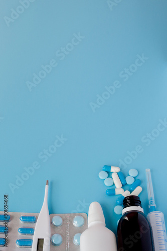 Treatment of colds and flu. Various medicines, a thermometer, sprays from a stuffy nose and a pain in a throat on a blue background. Copy space. Medicine flat lay