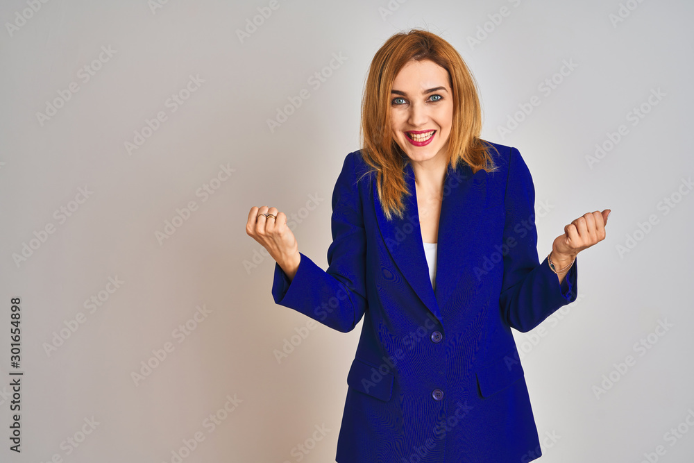 Redhead caucasian business woman wearing a suit over isolated background celebrating surprised and amazed for success with arms raised and open eyes. Winner concept. Redhead caucasian business woman wearing a suit over isolated background celebrating surprised and amazed for success with arms raised and open eyes. Winner concept.