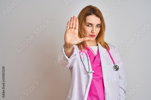 Redhead caucasian doctor woman wearing pink stethoscope over isolated background doing stop sing with palm of the hand. Warning expression with negative and serious gesture on the face.