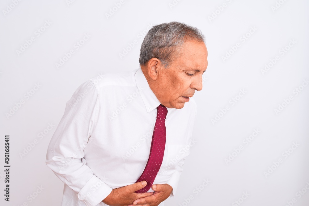 Senior grey-haired businessman wearing elegant tie over isolated white background with hand on stomach because indigestion, painful illness feeling unwell. Ache concept. Senior grey-haired businessman wearing elegant tie over isolated white background with hand on stomach because indigestion, painful illness feeling unwell. Ache concept.