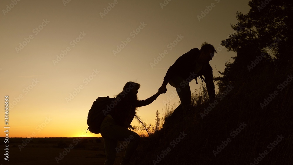 tourists go down from the goy in the sunset, holding hands. male traveler holds hand of a female traveler going down from top of the hill. teamwork of business people. Happy family on vacation.