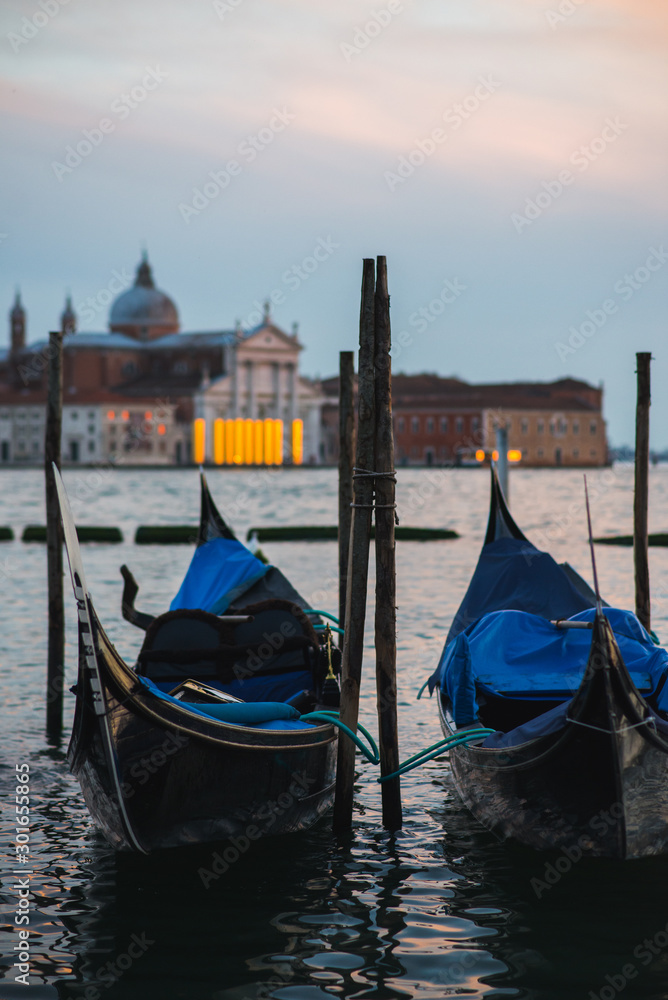 Traditional venetian gondolas by the waterfront. Several boats for travelers and tourists are covered with covers at the pier.