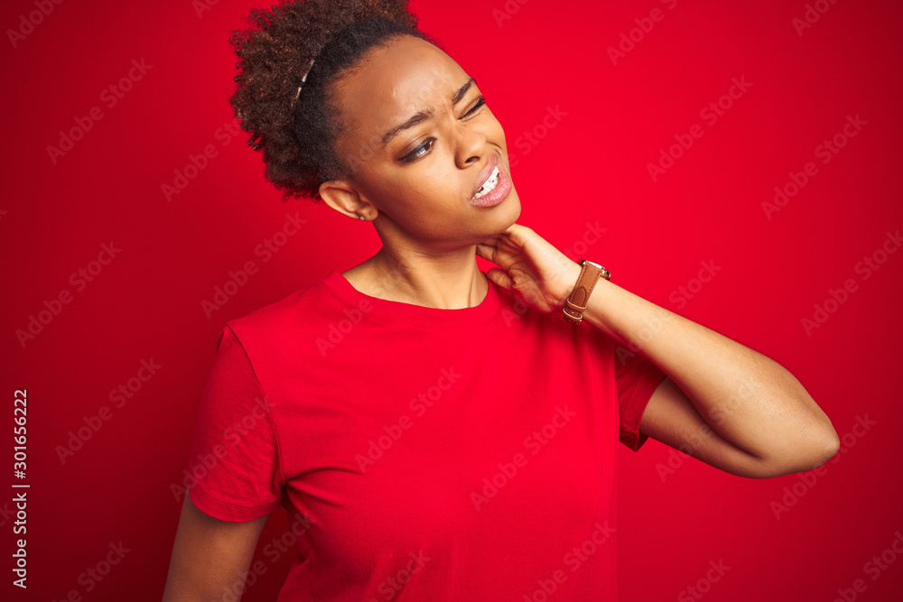 Young beautiful african american woman with afro hair over isolated red background Suffering of neck ache injury, touching neck with hand, muscular pain Young beautiful african american woman with afro hair over isolated red background Suffering of neck ache injury, touching neck with hand, muscular pain