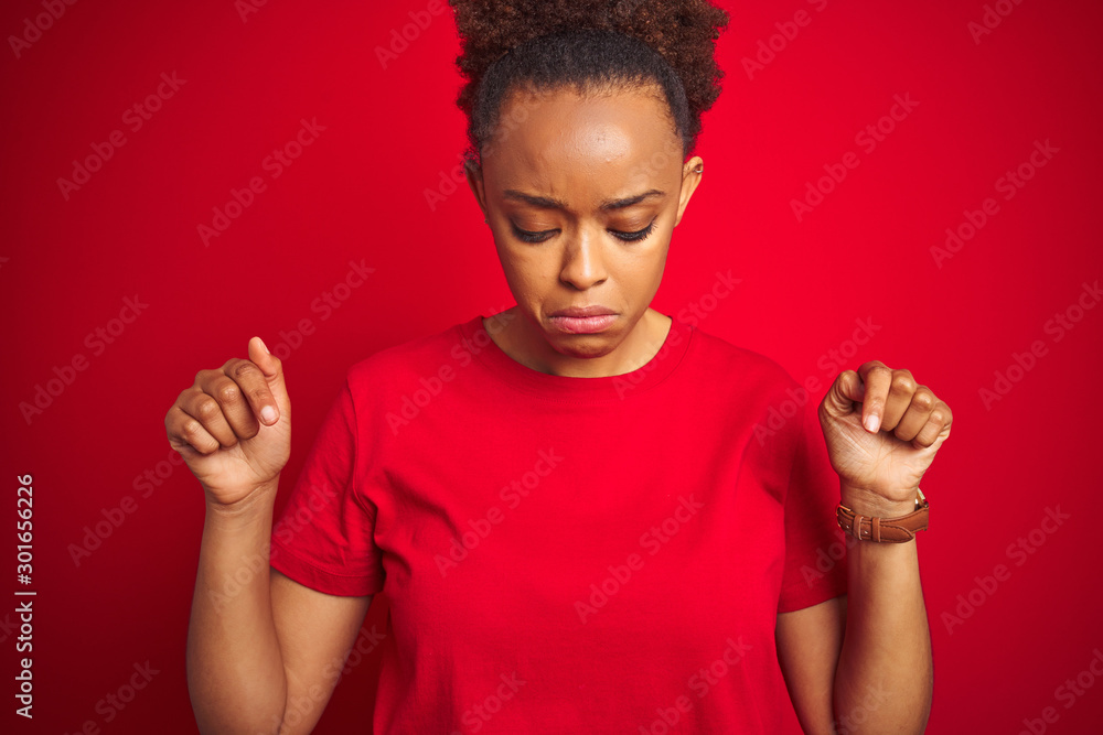 Young beautiful african american woman with afro hair over isolated red background Pointing down looking sad and upset, indicating direction with fingers, unhappy and depressed. Young beautiful african american woman with afro hair over isolated red background Pointing down looking sad and upset, indicating direction with fingers, unhappy and depressed.