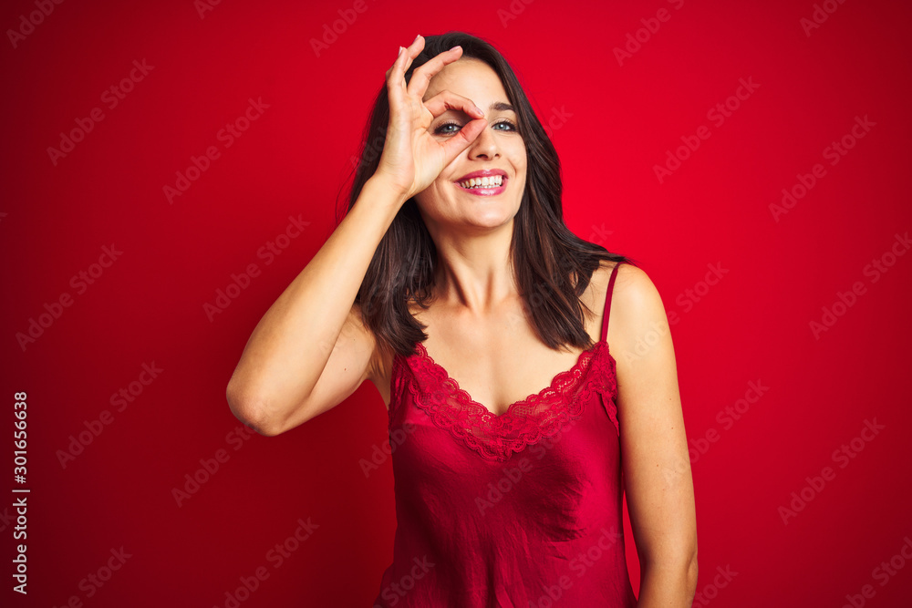 Young beautiful woman wearing sexy lingerie over red isolated background doing ok gesture with hand smiling, eye looking through fingers with happy face. Young beautiful woman wearing sexy lingerie over red isolated background doing ok gesture with hand smiling, eye looking through fingers with happy face.