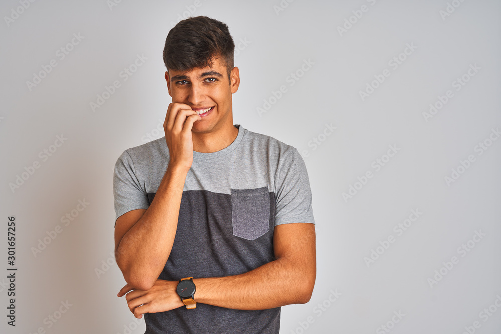 Young indian man wearing casual t-shirt standing over isolated white background looking stressed and nervous with hands on mouth biting nails. Anxiety problem.