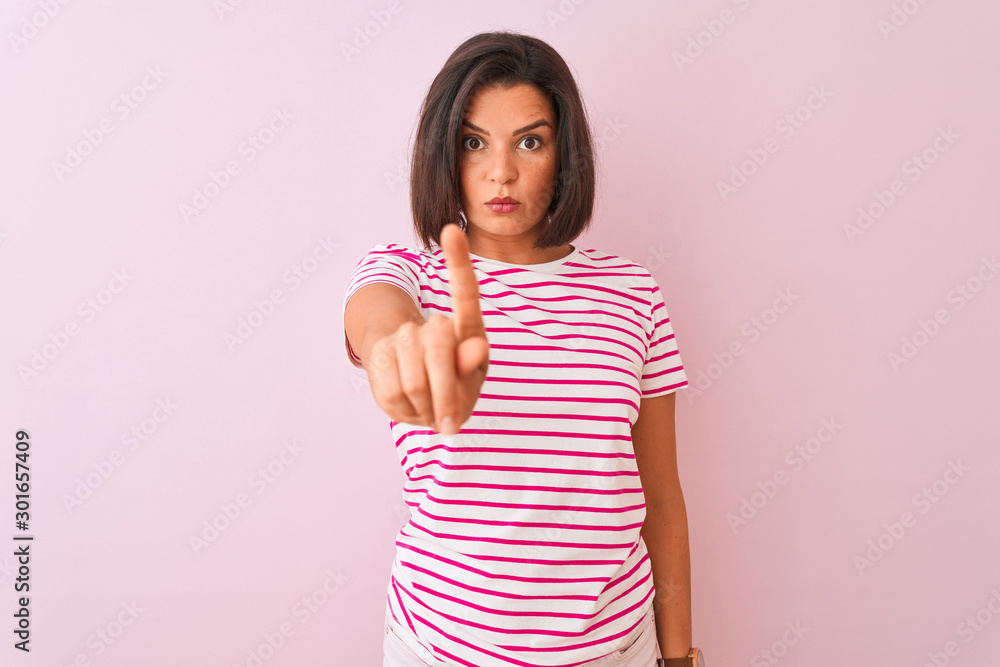 Young beautiful woman wearing striped t-shirt standing over isolated pink background Pointing with finger up and angry expression, showing no gesture Young beautiful woman wearing striped t-shirt standing over isolated pink background Pointing with finger up and angry expression, showing no gesture