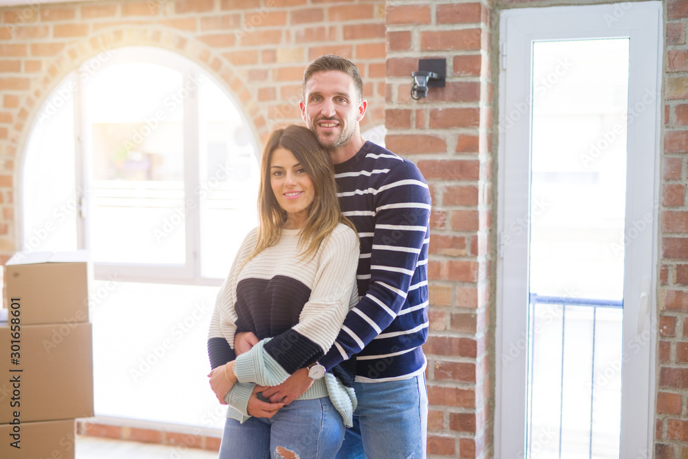 Young beautiful couple hugging at new home around cardboard boxes Young beautiful couple hugging at new home around cardboard boxes