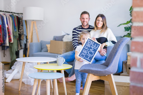 Beautiful famiily with kid sitting on the sofa holding blackboard at new home around cardboard boxes photo