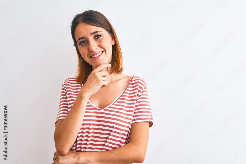 Beautiful redhead woman wearing casual striped red t-shirt over isolated background looking confident at the camera smiling with crossed arms and hand raised on chin. Thinking positive. Beautiful redhead woman wearing casual striped red t-shirt over isolated background looking confident at the camera smiling with crossed arms and hand raised on chin. Thinking positive.