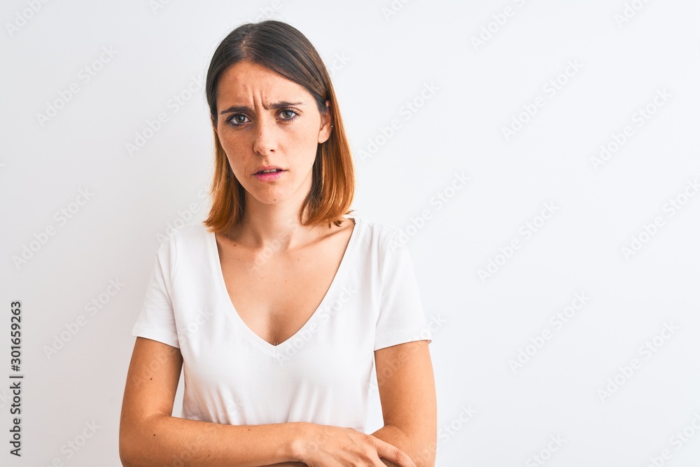 Beautiful redhead woman wearing casual white t-shirt over isolated background skeptic and nervous, disapproving expression on face with crossed arms. Negative person. Beautiful redhead woman wearing casual white t-shirt over isolated background skeptic and nervous, disapproving expression on face with crossed arms. Negative person.