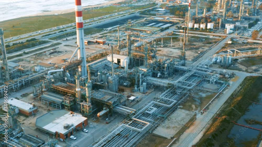 Aerial view of petrochemical oil refinery (refining complex) on the ocean coastline at sunset. Oil and gas tanks with fuming pipes on the plant (factory) Aerial view of petrochemical oil refinery (refining complex) on the ocean coastline at sunset. Oil and gas tanks with fuming pipes on the plant (factory)