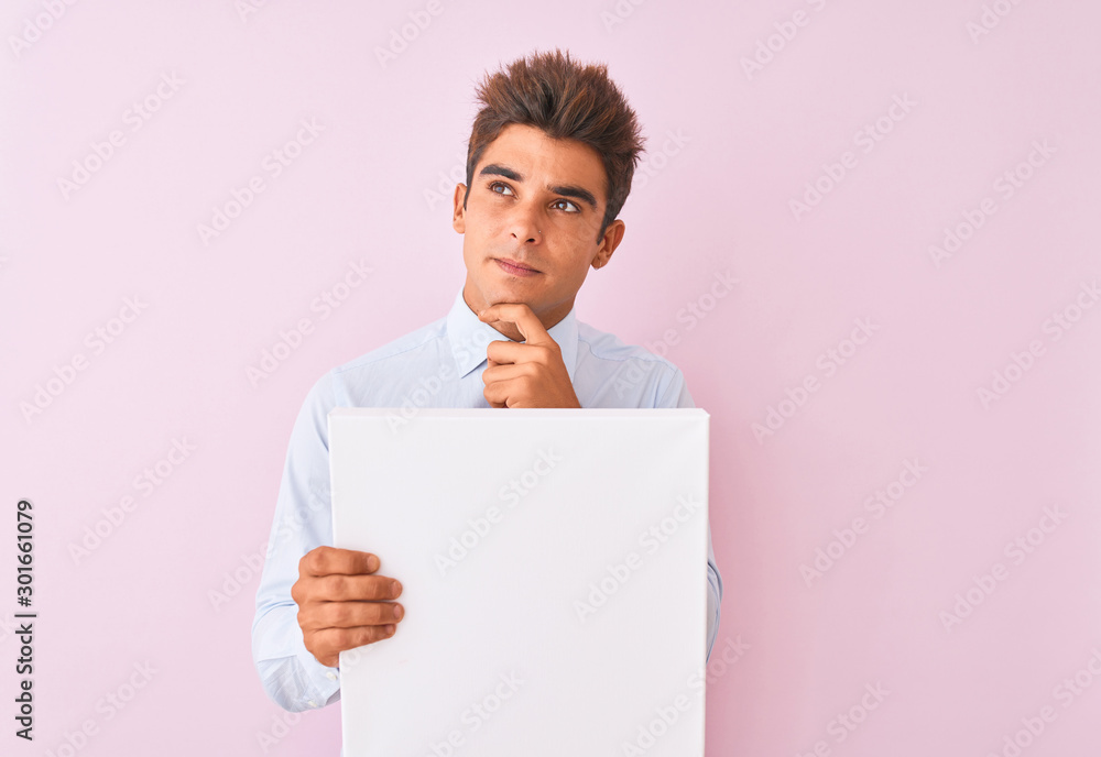 Young handsome businessman holding banner standing over isolated pink background serious face thinking about question, very confused idea Young handsome businessman holding banner standing over isolated pink background serious face thinking about question, very confused idea