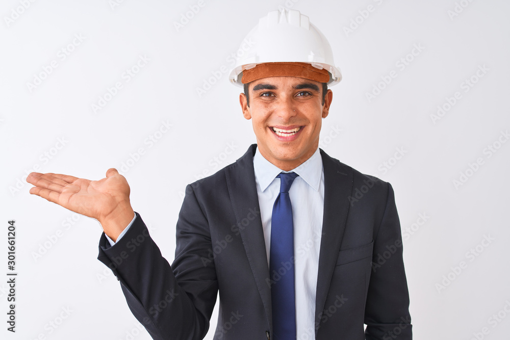 Young handsome architect man wearing suit and helmet over isolated white background smiling cheerful presenting and pointing with palm of hand looking at the camera. Young handsome architect man wearing suit and helmet over isolated white background smiling cheerful presenting and pointing with palm of hand looking at the camera.