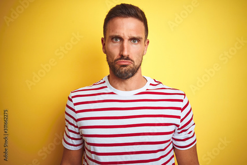 Young handsome man wearing casual red striped t-shirt over yellow isolated background depressed and worry for distress  crying angry and afraid. Sad expression.