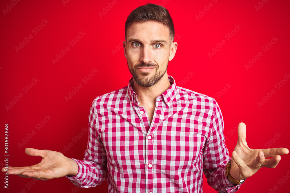 Fototapeta premium Young handsome man over red isolated background clueless and confused with open arms, no idea concept.