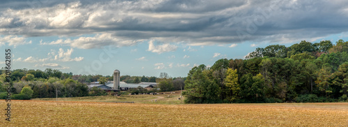 Panaramic view of a farm with cows and a silo surrounded by a field and woods