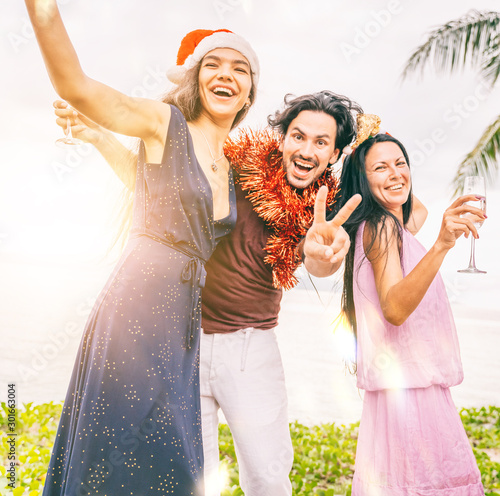 Group of happy people of mixed race friends celebrate Christmas and New Year at a tropical resort in Santa hats with glasses of champagne in their hands