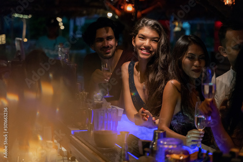 A party of friends in a nightclub at the bar, glamorous young people relax with alcohol