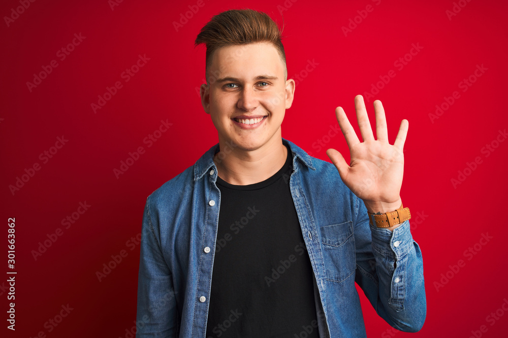 Young handsome man wearing denim shirt standing over isolated red background showing and pointing up with fingers number five while smiling confident and happy. Young handsome man wearing denim shirt standing over isolated red background showing and pointing up with fingers number five while smiling confident and happy.