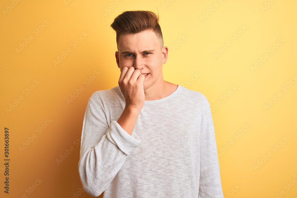 Young handsome man wearing white casual t-shirt standing over isolated yellow background looking stressed and nervous with hands on mouth biting nails. Anxiety problem. Young handsome man wearing white casual t-shirt standing over isolated yellow background looking stressed and nervous with hands on mouth biting nails. Anxiety problem.