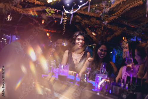 A party of friends in a nightclub at the bar, glamorous young people relax with alcohol