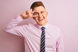 Young handsome businessman wearing shirt and tie standing over isolated pink background Doing peace symbol with fingers over face, smiling cheerful showing victory