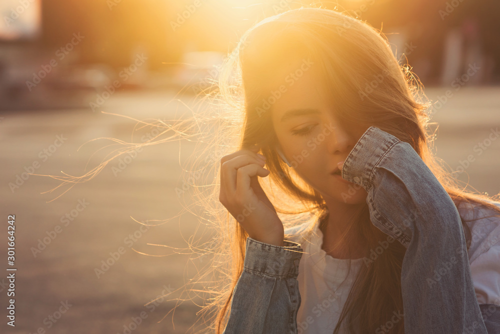 Back light portrait of a happy single teen girl breathing fresh air in a city street during a sunny day at sunset in a park with a warm yellow light and urban background. Summertime. Lifestyle. - obrazy, fototapety, plakaty 