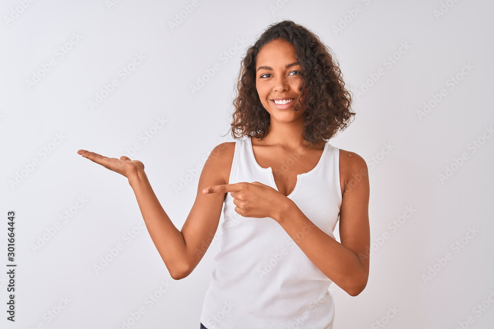 Young brazilian woman wearing casual t-shirt standing over isolated white background amazed and smiling to the camera while presenting with hand and pointing with finger. Young brazilian woman wearing casual t-shirt standing over isolated white background amazed and smiling to the camera while presenting with hand and pointing with finger.