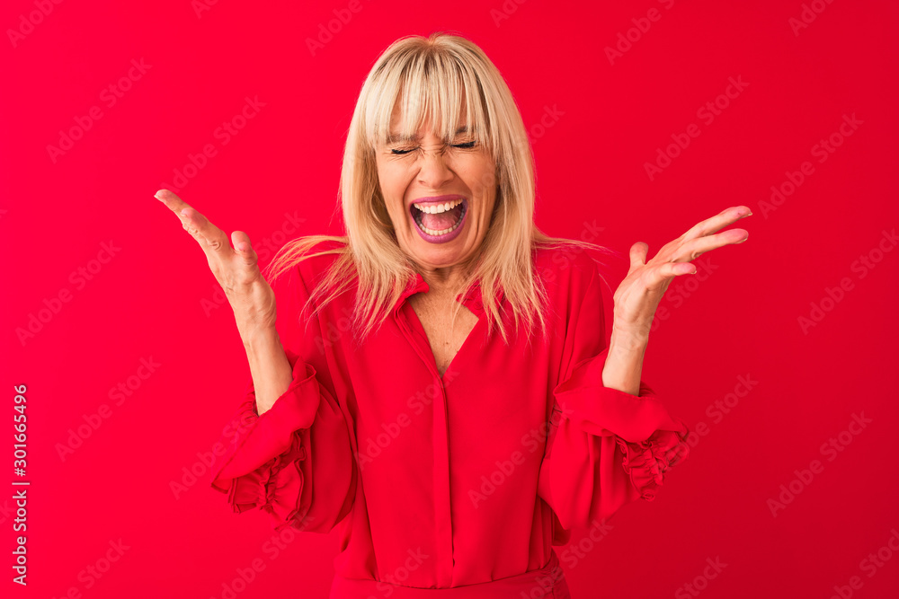 Middle age woman wearing elegant shirt standing over isolated red background celebrating mad and crazy for success with arms raised and closed eyes screaming excited. Winner concept Middle age woman wearing elegant shirt standing over isolated red background celebrating mad and crazy for success with arms raised and closed eyes screaming excited. Winner concept