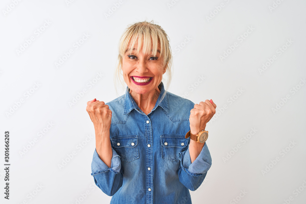 Middle age woman wearing casual denim shirt standing over isolated white background celebrating surprised and amazed for success with arms raised and open eyes. Winner concept. - obrazy, fototapety, plakaty 