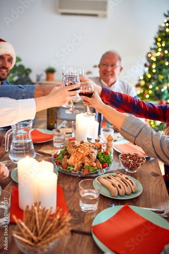 Beautiful family wearing santa claus hat meeting smiling happy and confident. Eating roasted turkey toasting with cup of wine celebrating Christmas at home