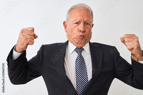 Senior grey-haired businessman wearing suit standing over isolated white background showing arms muscles smiling proud. Fitness concept.