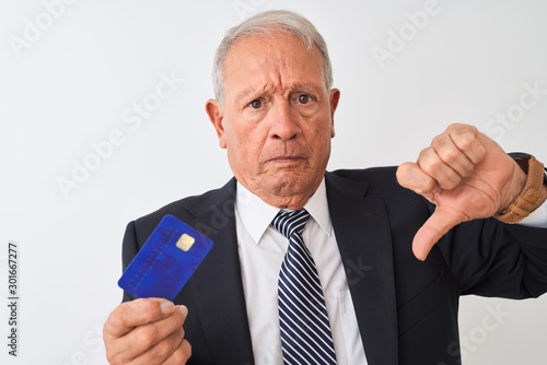 Senior grey-haired businessman holding credit card over isolated white background with angry face, negative sign showing dislike with thumbs down, rejection concept © Krakenimages.com