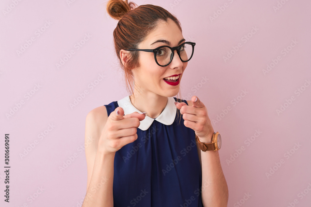 Redhead woman with pigtail wearing elegant dress and glasses over isolated pink background pointing fingers to camera with happy and funny face. Good energy and vibes. Redhead woman with pigtail wearing elegant dress and glasses over isolated pink background pointing fingers to camera with happy and funny face. Good energy and vibes.