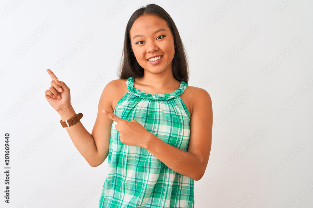 Young chinese woman wearing green dress standing over isolated white background smiling and looking at the camera pointing with two hands and fingers to the side. Young chinese woman wearing green dress standing over isolated white background smiling and looking at the camera pointing with two hands and fingers to the side.