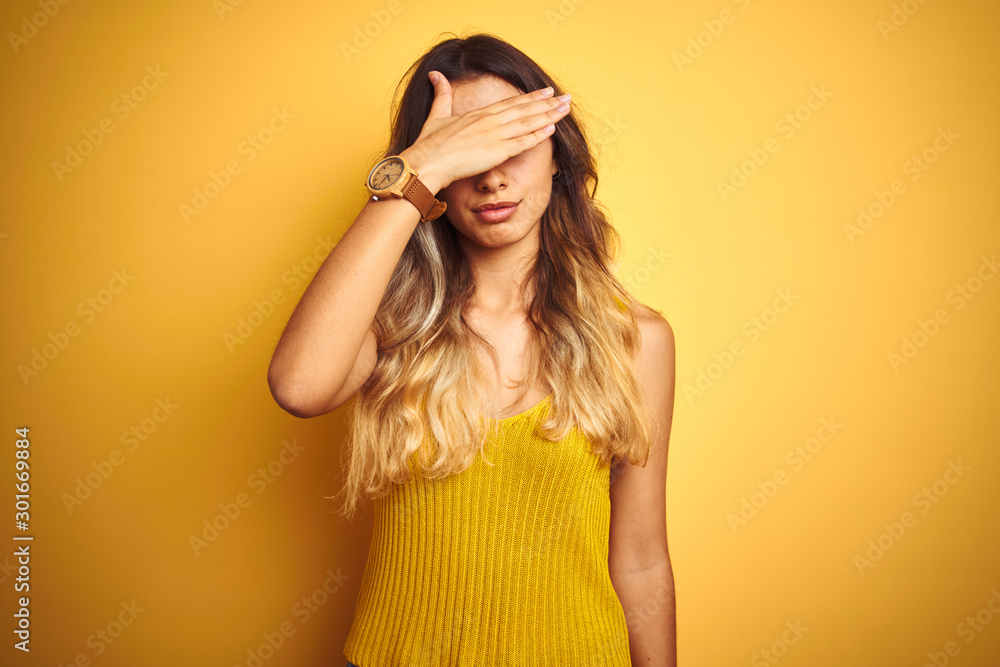 Young beautiful woman wearing t-shirt over yellow isolated background covering eyes with hand, looking serious and sad. Sightless, hiding and rejection concept