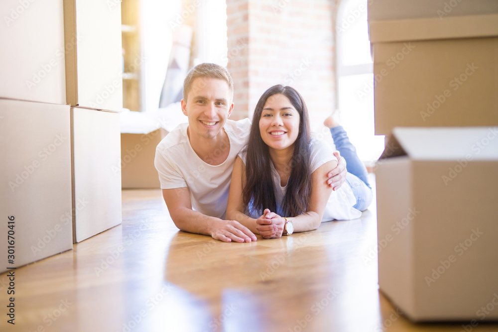 Young beautiful couple lying down at new home around cardboard boxes