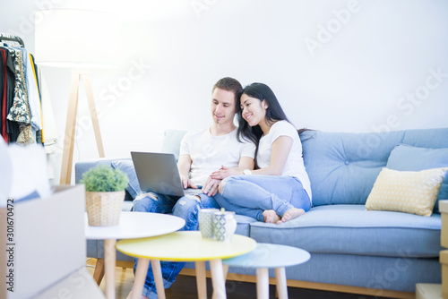 Young beautiful couple sitting on the sofa using laptop at new home around cardboard boxes