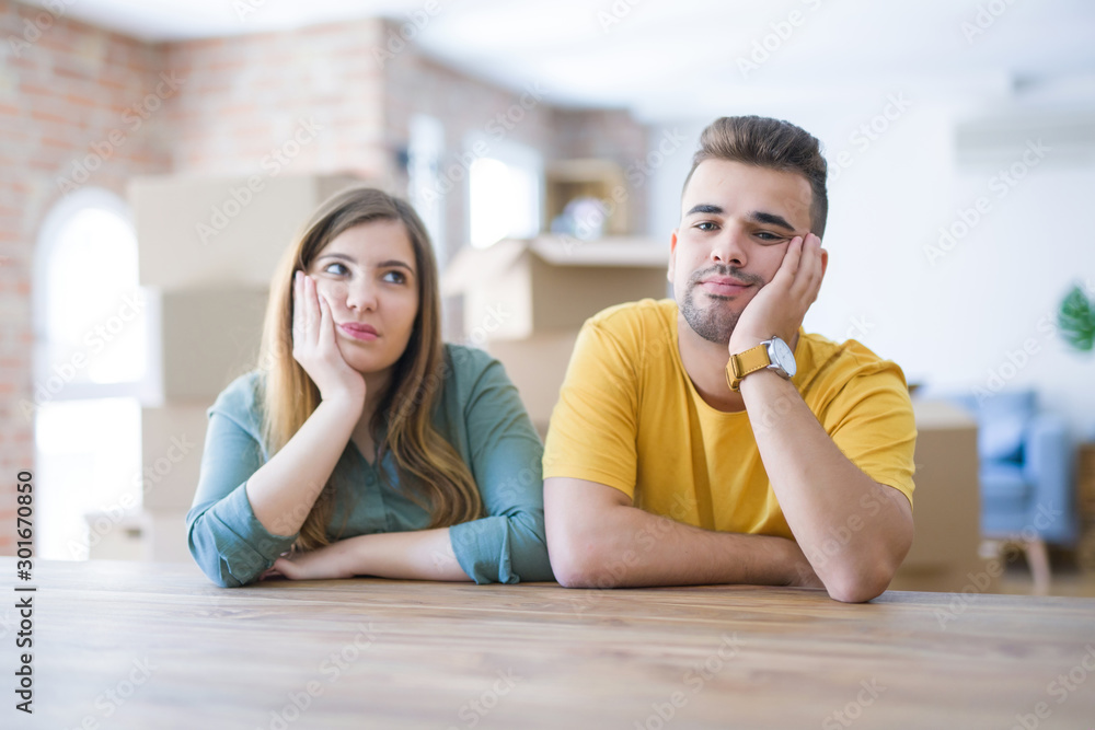 Young couple sitting on the table movinto to new home with carboard boxes behind them thinking looking tired and bored with depression problems with crossed arms. Young couple sitting on the table movinto to new home with carboard boxes behind them thinking looking tired and bored with depression problems with crossed arms.