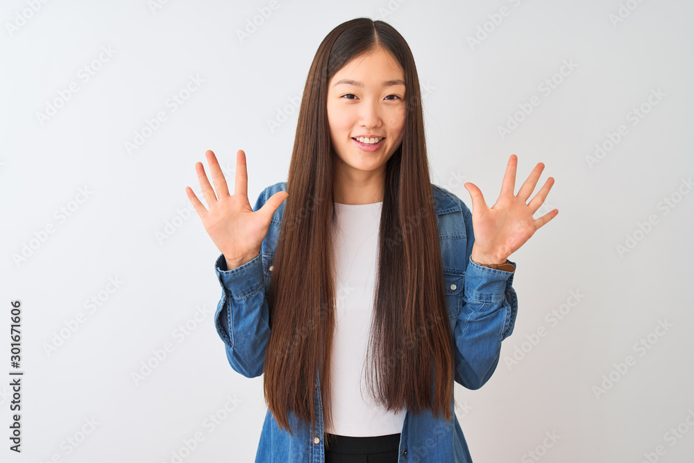 Young chinese woman wearing denim shirt standing over isolated white background showing and pointing up with fingers number ten while smiling confident and happy. Young chinese woman wearing denim shirt standing over isolated white background showing and pointing up with fingers number ten while smiling confident and happy.
