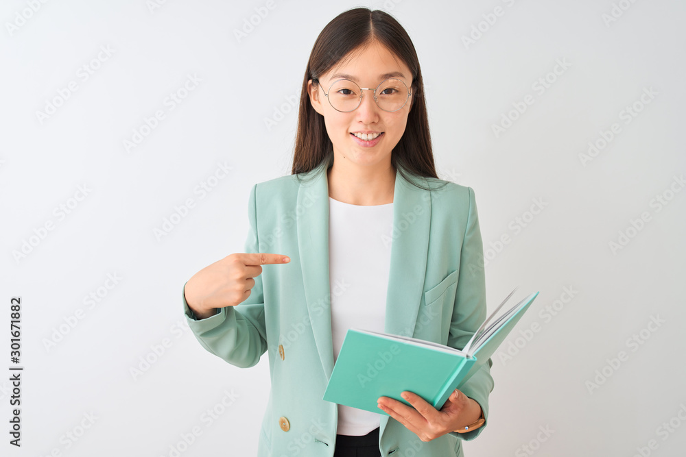 Young chinese student woman wearing glasses reading book over isolated white background with surprise face pointing finger to himself Young chinese student woman wearing glasses reading book over isolated white background with surprise face pointing finger to himself