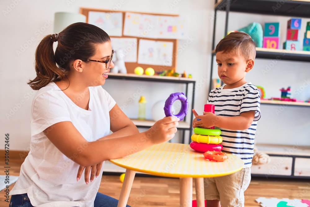 Beautiful teacher and toddler boy building pyramid with hoops bolcks at kindergarten